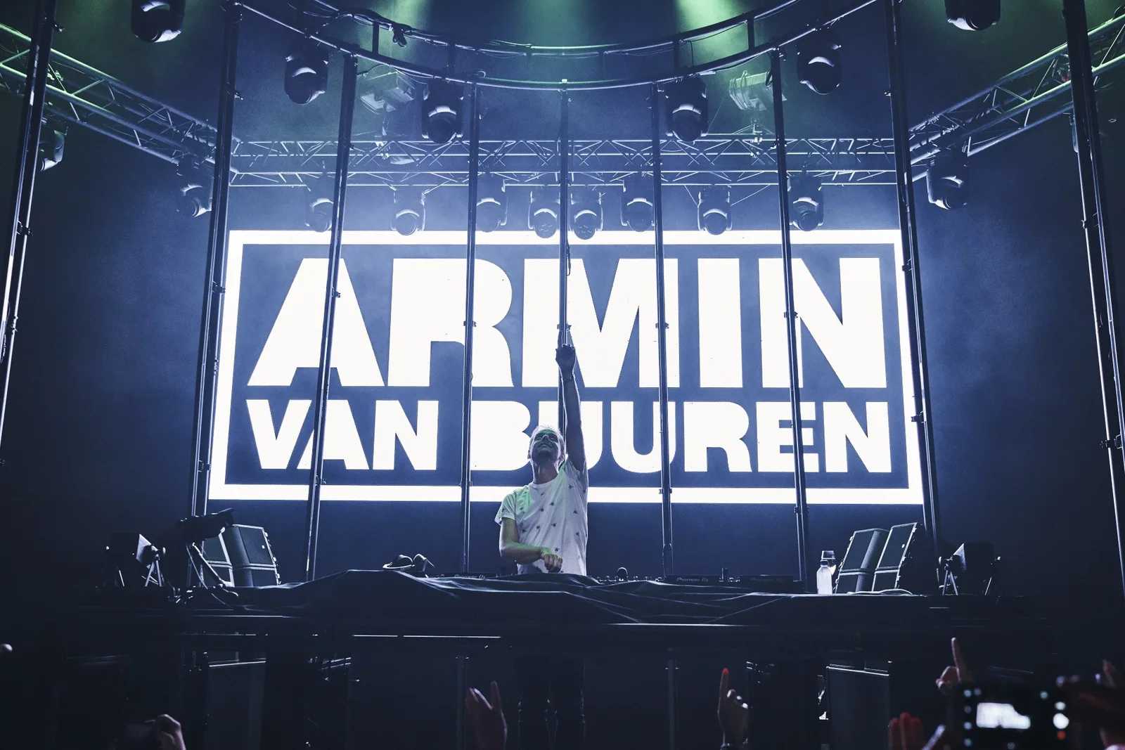 DJ mit erhobenem Arm vor einer leuchtenden Bühnenwand mit dem Namen Armin van Buuren