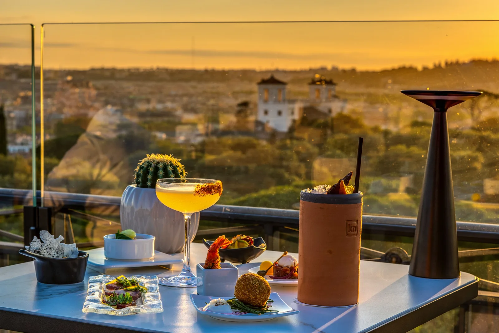 Cocktails und kleine Gerichte auf einem Tisch der Dachterrasse im Abendlicht