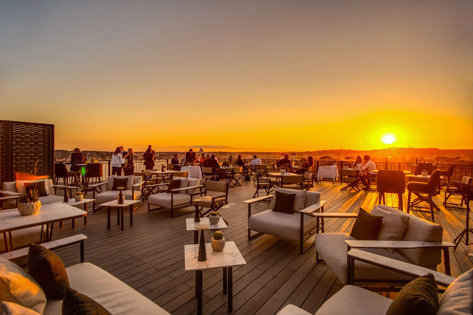 Gäste auf der Dachterrasse mit Loungemöbeln beim Sonnenuntergang