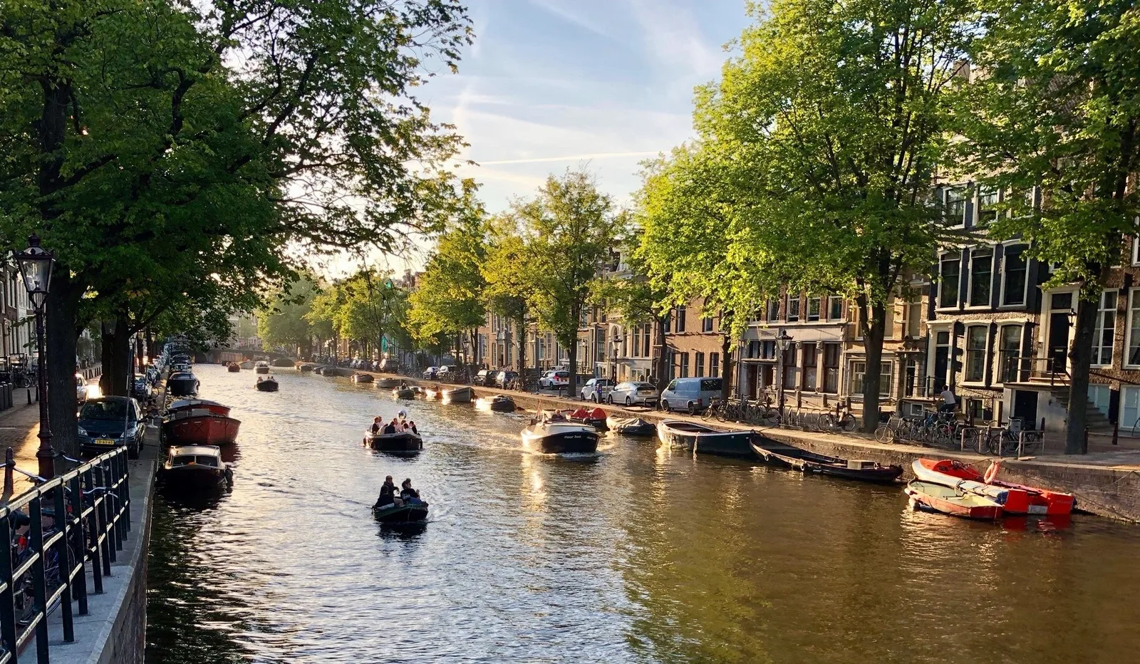 Amsterdamer Gracht im Abendlicht mit kleinen Booten, Bäumen und Grachtenhäusern am Ufer