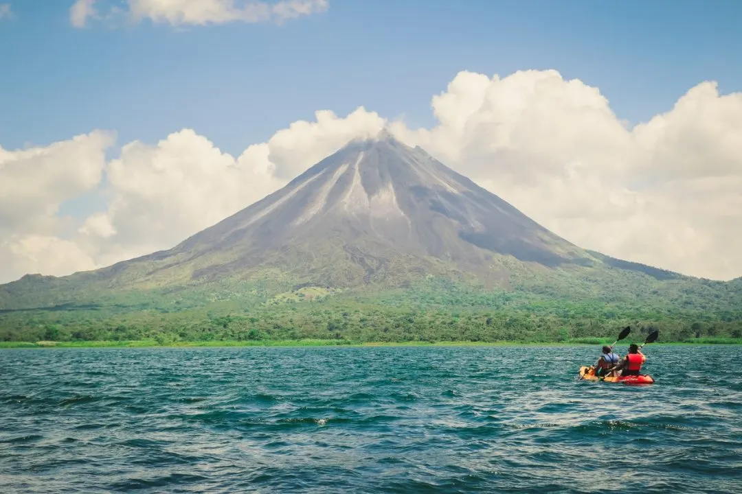 Zwei Menschen im Kajak auf dem Arenal-See vor dem kegelförmigen Vulkan Arenal