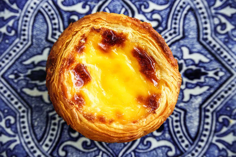 Pastel de Nata mit gebräunter Puddingfüllung von oben auf blau gemusterten Fliesen
