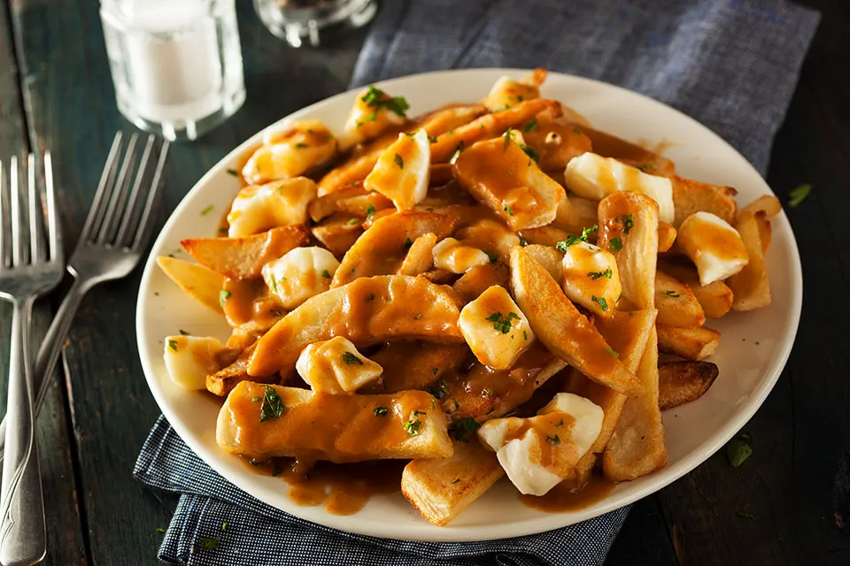 Teller Poutine: Pommes mit Käsestücken und dunkler Bratensauce, daneben zwei Gabeln