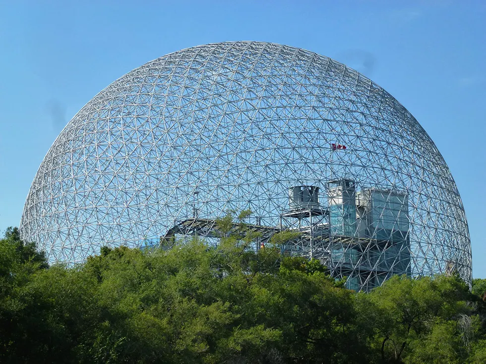 Geodätische Stahlkuppel der Biosphère über Baumwipfeln vor blauem Himmel