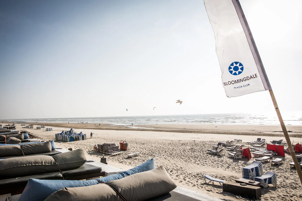 Liegen mit Kissen auf der Terrasse des Bloomingdale Beach Club, davor der weite Sandstrand und die Nordsee