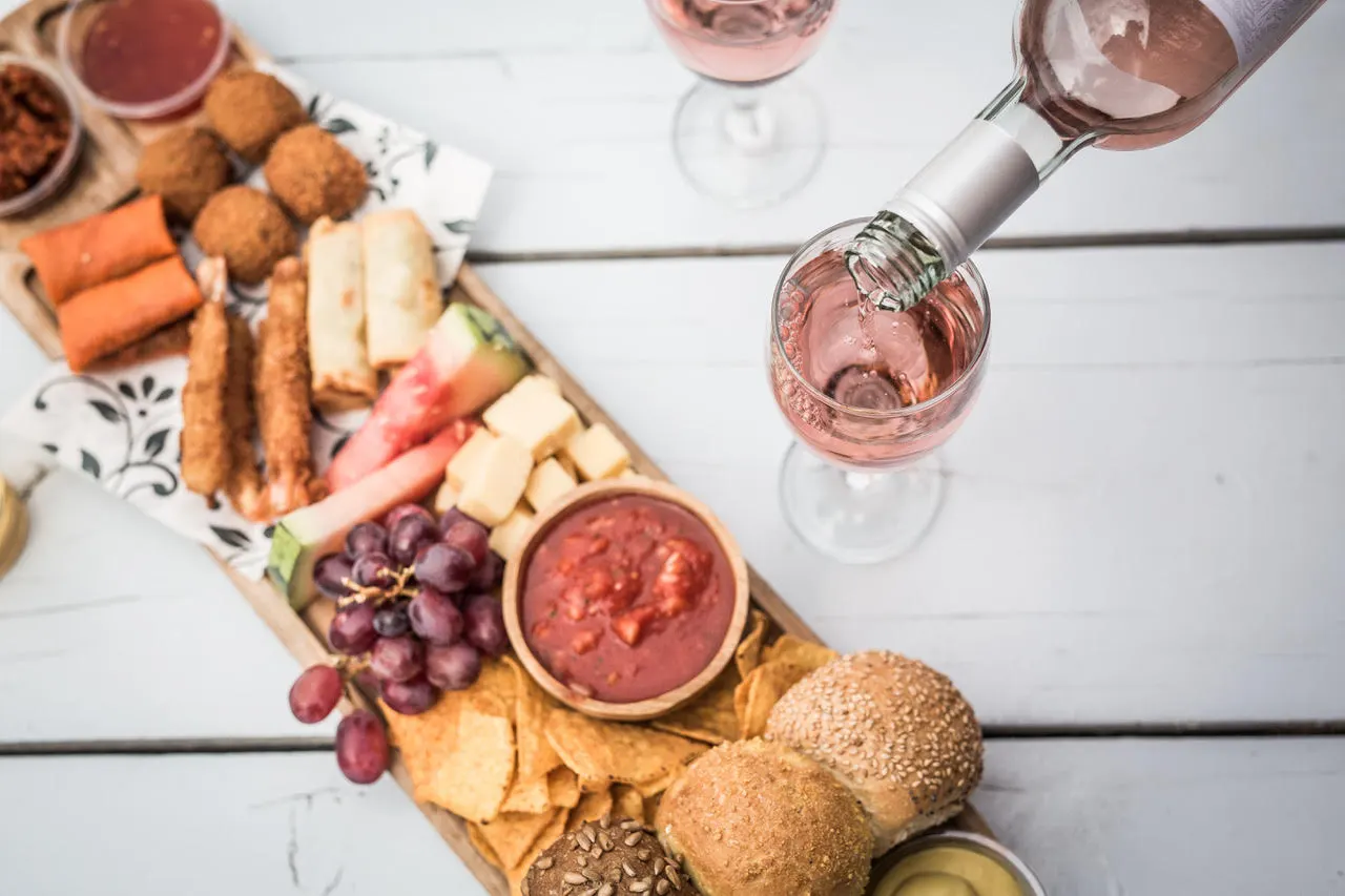 Holzbrett mit Bitterballen, Käse, Trauben und Salsa, daneben wird Rosé eingeschenkt