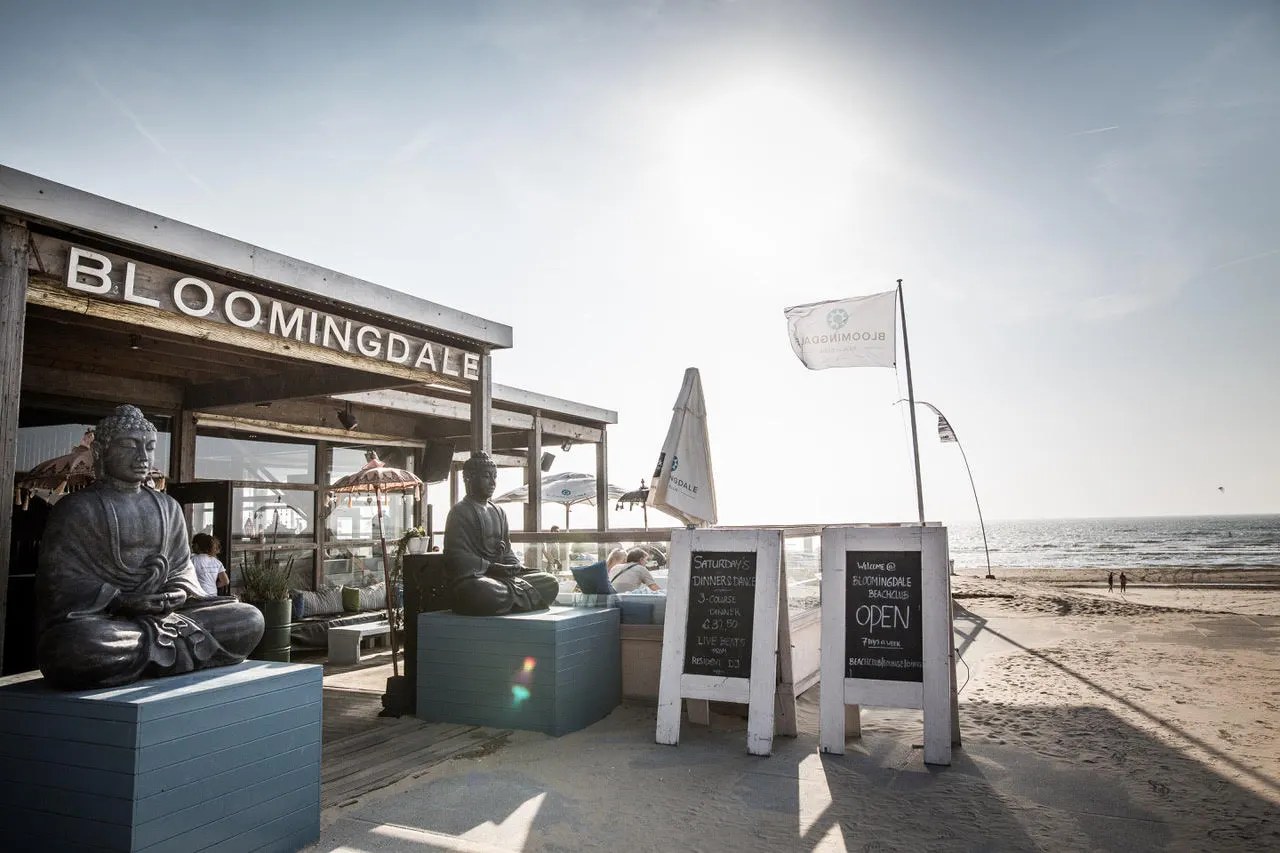 Holzpavillon mit Schriftzug „Bloomingdale“, Buddha-Figuren und Tafel „Open“ am Strand