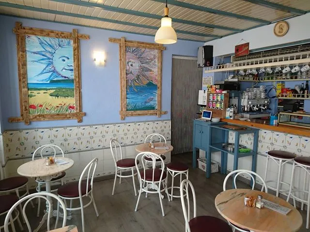 Gastraum des Cafés mit blau gestrichenen Wänden, gerahmten Sonnenbildern und weißen Bistrostühlen