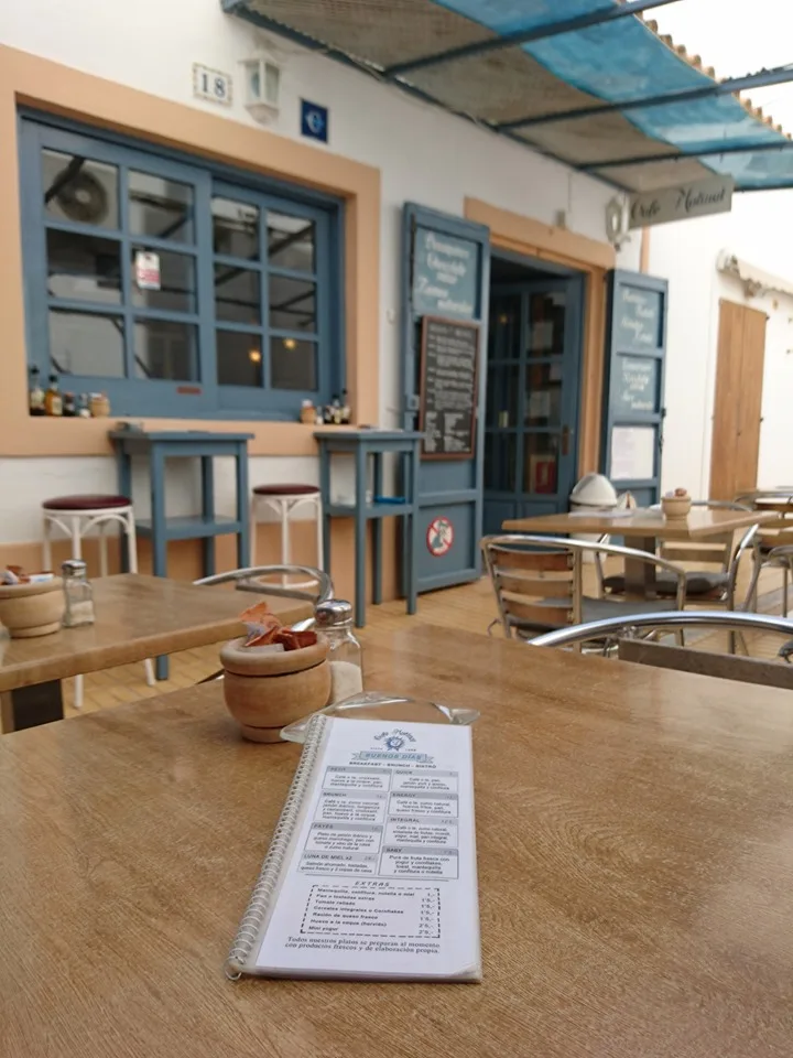 Blick vom Tisch der Terrasse auf den blau gerahmten Eingang des Cafés, im Vordergrund die Speisekarte