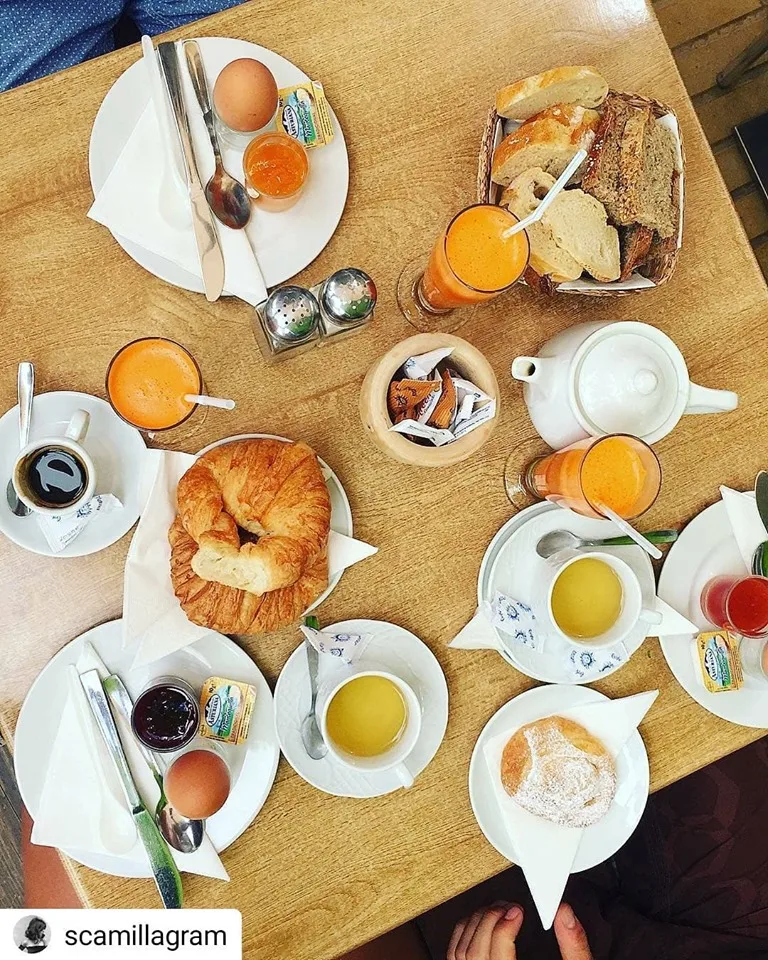 Frühstückstisch von oben mit Croissant, gekochten Eiern, Brotkorb, Kaffee und frisch gepressten Säften