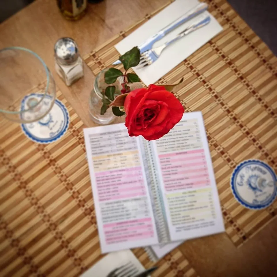 Gedeckter Tisch mit aufgeschlagener Speisekarte und einer roten Rose in der Vase