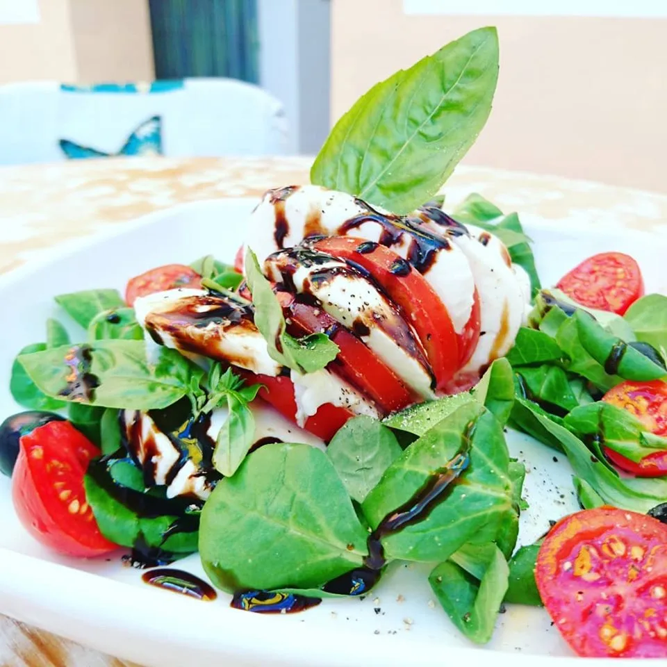 Teller mit Tomaten-Mozzarella-Salat, Basilikumblättern und Balsamico