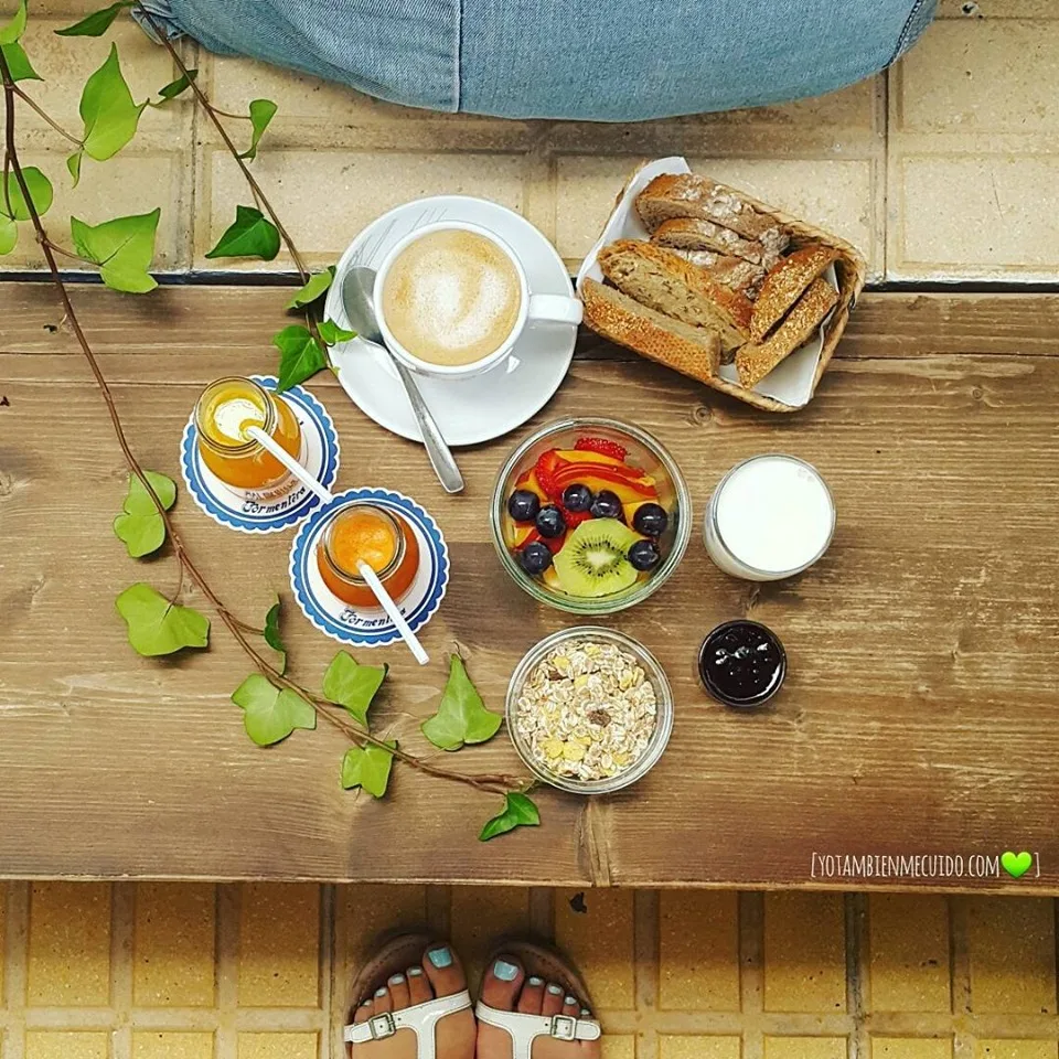 Frühstück von oben mit Milchkaffee, Brotkorb, Obstschale und Müsli auf einer Holzbank