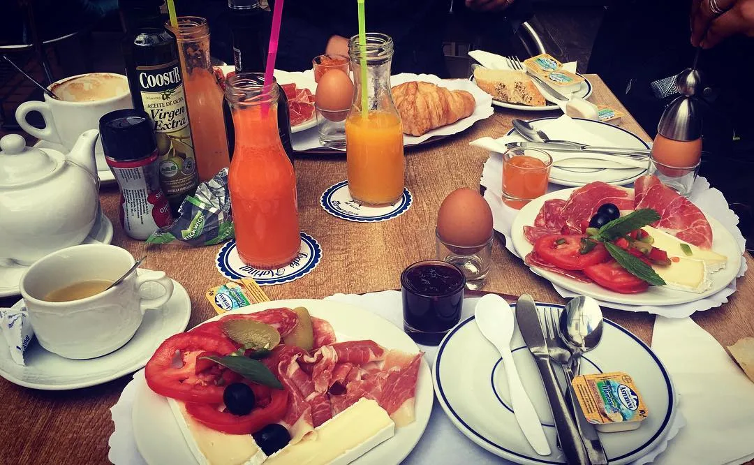 Gedeckter Frühstückstisch mit Schinken-Käse-Tellern, Croissant, Eiern und Saftflaschen