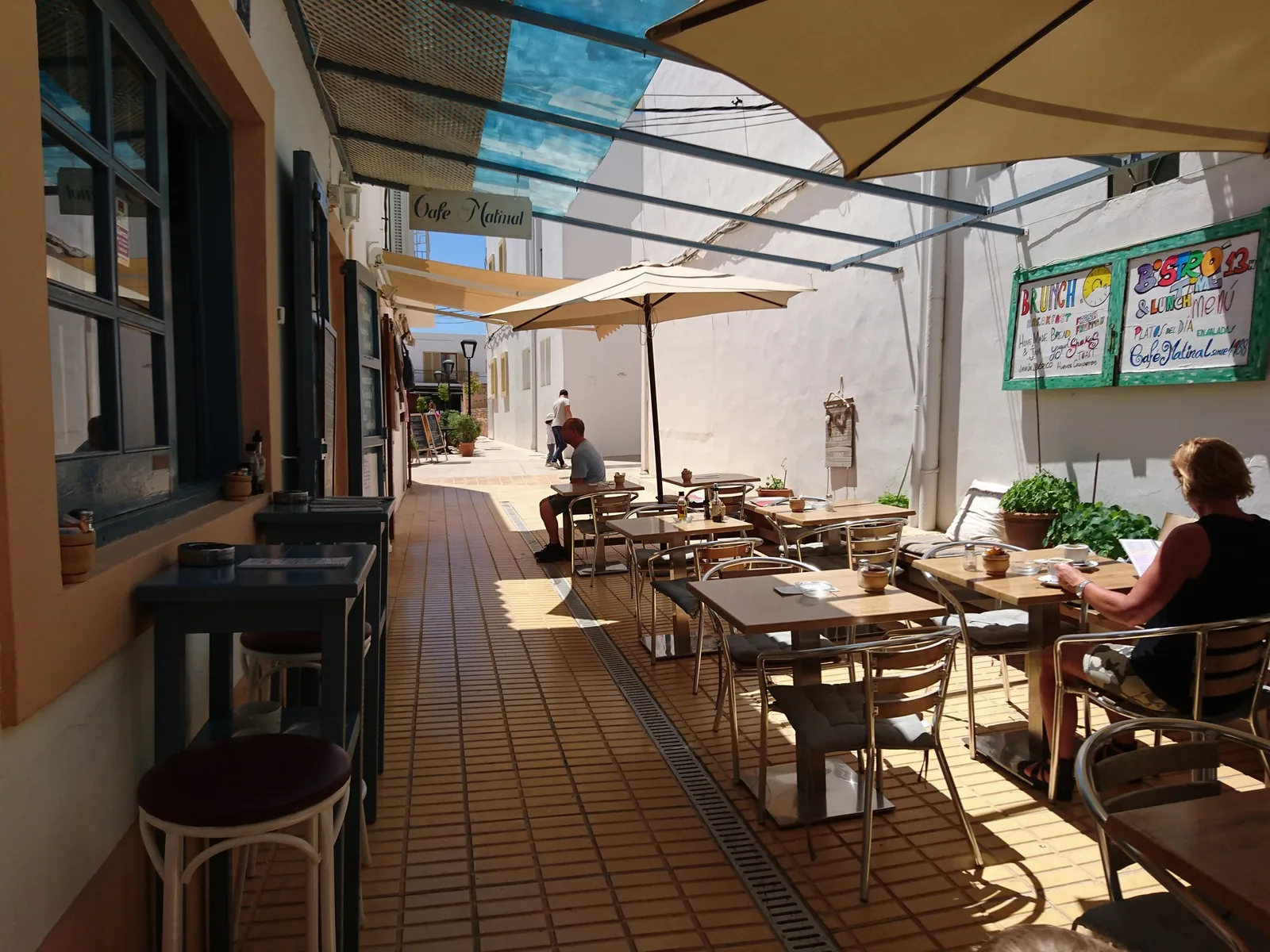 Terrasse in einer schmalen Gasse mit Sonnenschirmen, Tischen und Gästen beim Frühstück