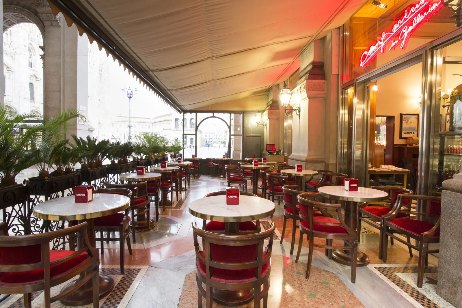 Terrasse unter einer Markise mit Marmortischen und roten Polsterstühlen neben dem Domplatz