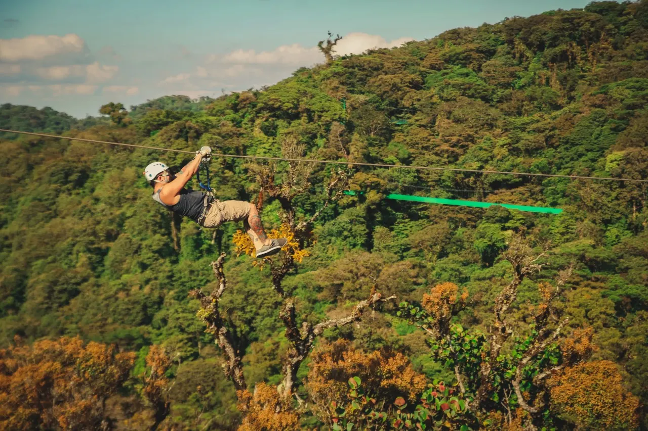 Mann gleitet an der Zipline über die Baumkronen, dahinter eine grüne Plattform