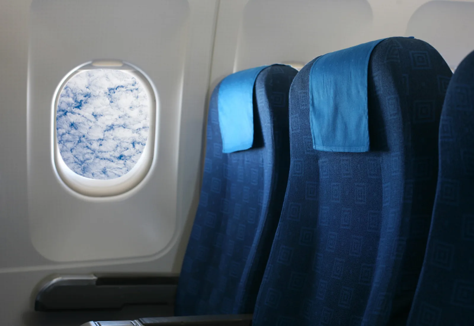Blick auf eine Reihe blauer Flugzeugsitze neben einem Kabinenfenster mit Wolken
