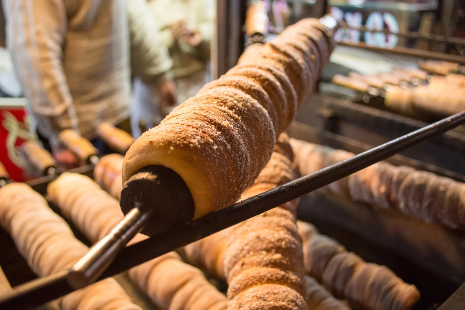 Trdelník-Teigrollen mit Zuckerkruste drehen sich am Spieß über der Glut eines Marktstands