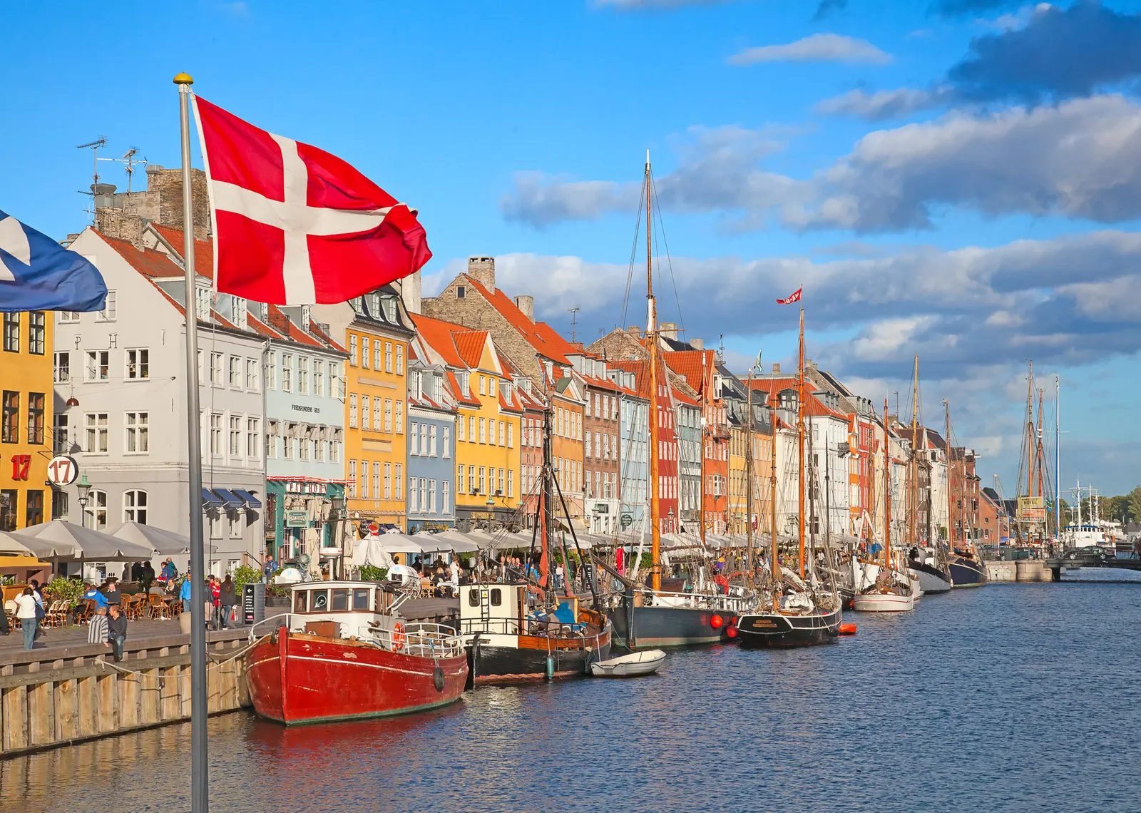 Bunte Giebelhäuser und Segelboote am Kopenhagener Kanal Nyhavn, davor die dänische Flagge