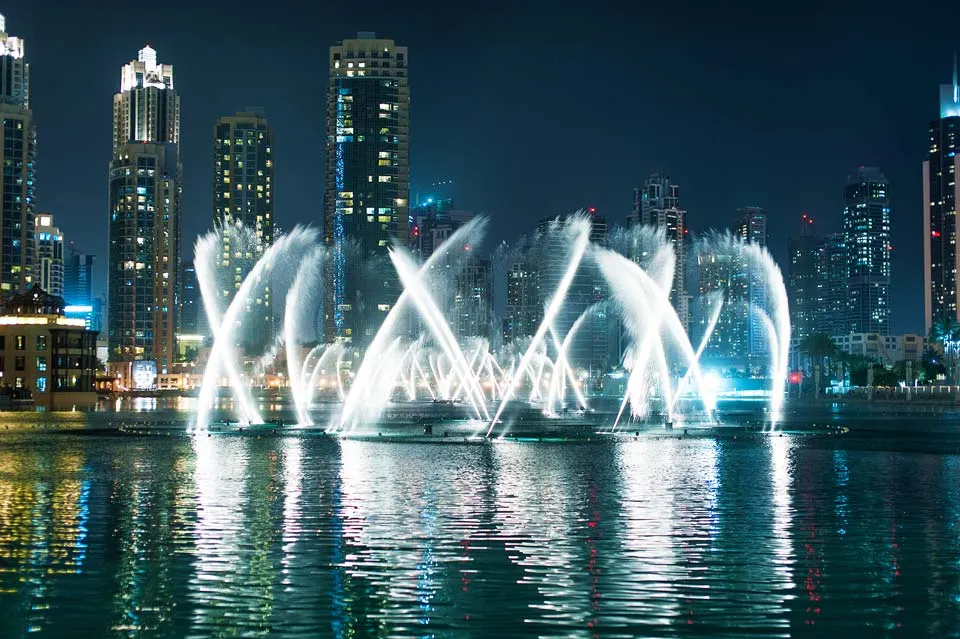 Beleuchtete Wasserfontänen über dem See vor der nächtlichen Skyline von Dubai
