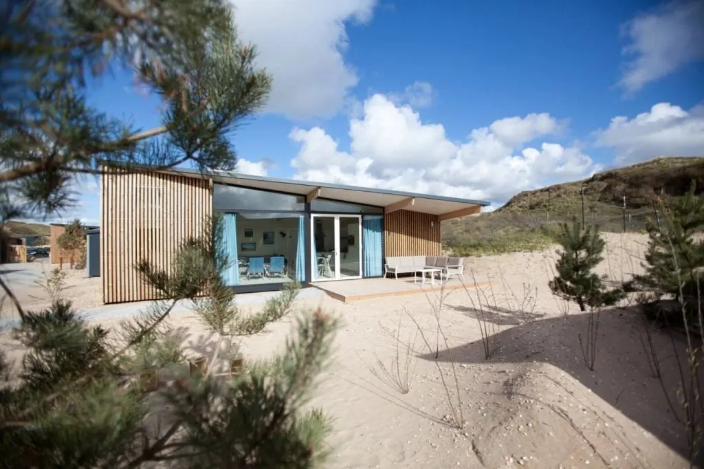 Dünenhaus mit Holzlattenfassade und blauen Vorhängen zwischen Kiefern und Sand in Bloemendaal