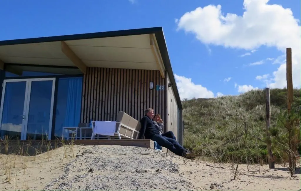 Paar sitzt auf dem Sandhügel vor einem Dünenhaus in Bloemendaal unter blauem Himmel