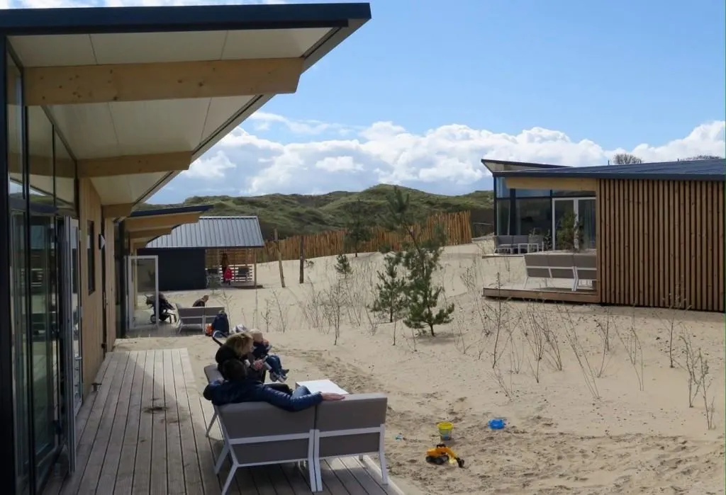 Holzterrasse zwischen Dünenhäusern in Bloemendaal, Gäste in Loungesesseln, Sandspielzeug im Vordergrund