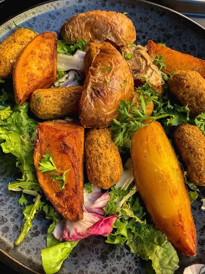 Frittierte Linsenröllchen und Kartoffelspalten auf Blattsalat, dazu ein Klecks Dip