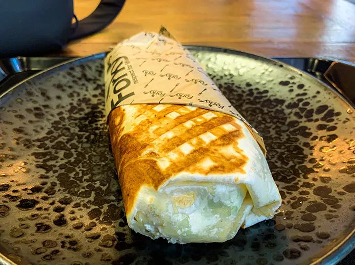 Gegrillter Wrap in bedrucktem Papier auf dunkel gesprenkeltem Teller, Füllung angeschnitten sichtbar