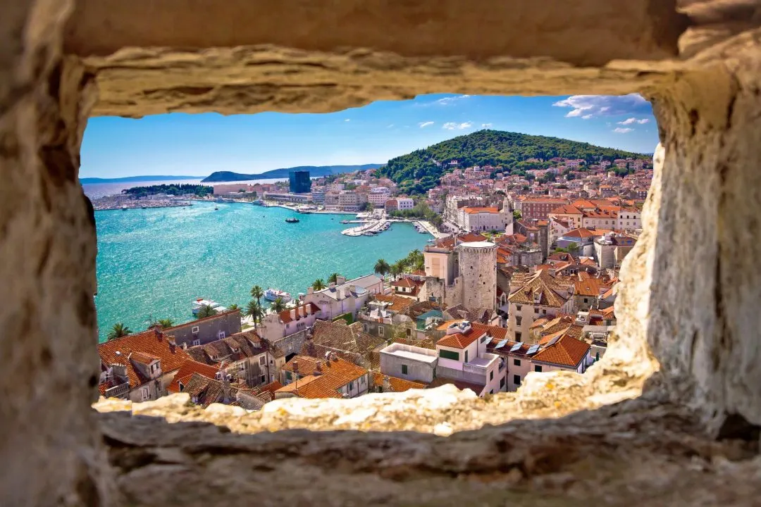 Blick durch ein Mauerfenster über die roten Dächer von Split und den Hafen