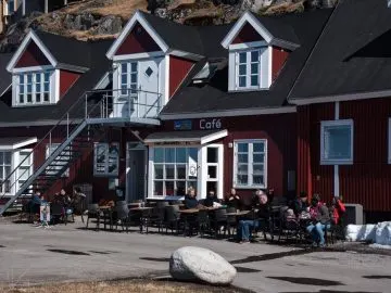 Gäste sitzen draußen vor einem rot gestrichenen Holzhaus mit Schild Café in Grönland