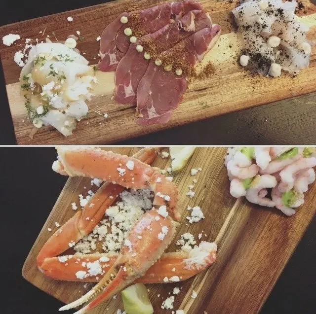 Zwei Holzbretter mit rohem Fisch, Trockenfleisch, Krabbenbeinen und Garnelen im Café Toqqorfik