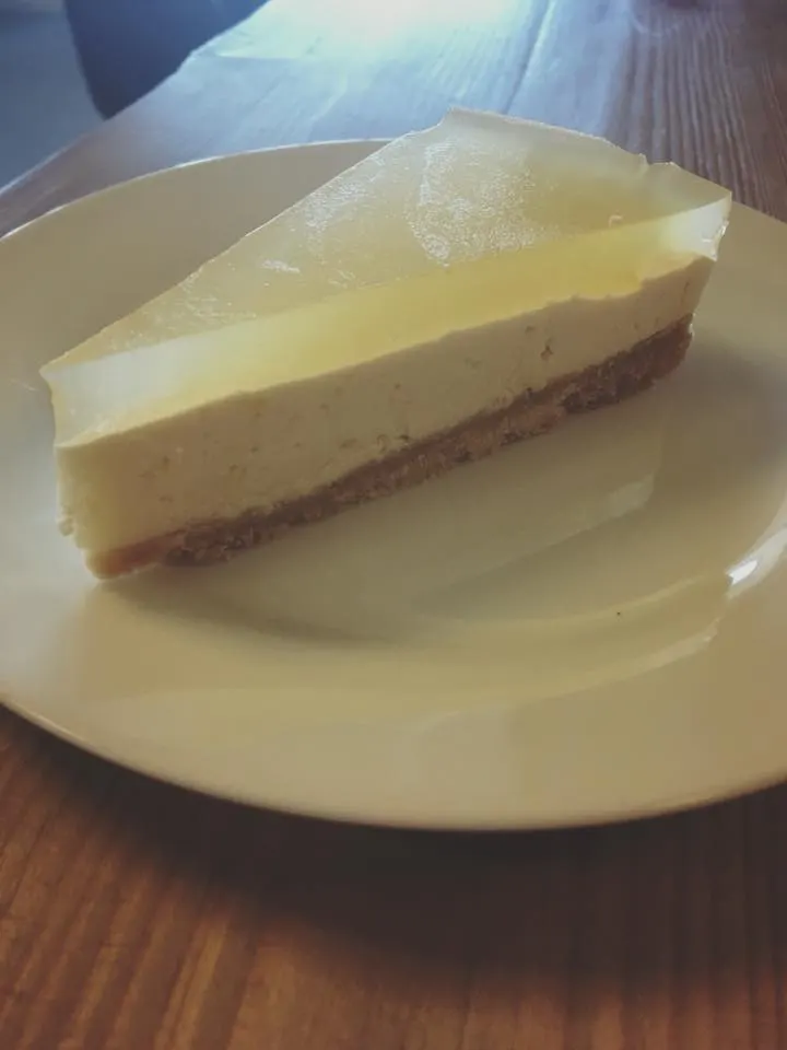 Stück Käsekuchen mit heller Glasur auf weißem Teller im Café Toqqorfik