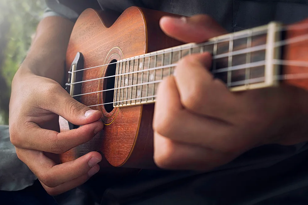 Nahaufnahme von Händen, die auf einer hölzernen Ukulele einen Akkord greifen