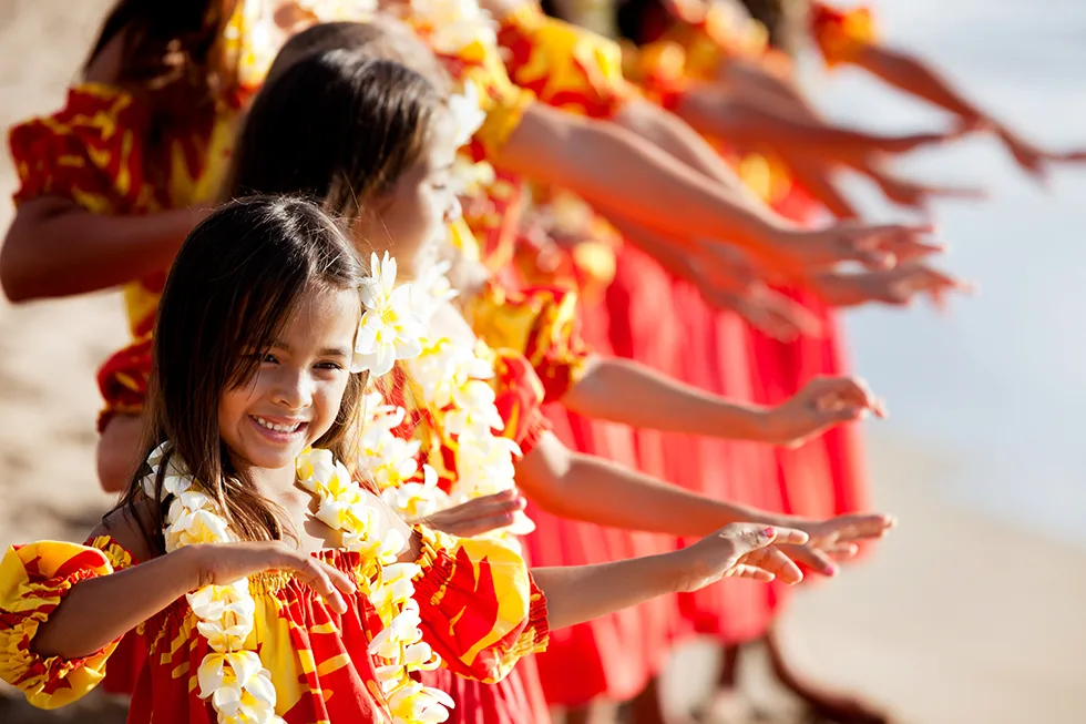 Mädchen in roten Hula-Kostümen mit Blumenketten tanzen am Strand in einer Reihe