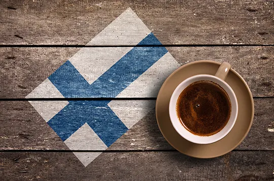 Tasse schwarzer Kaffee neben einer auf Holzbretter gemalten finnischen Flagge
