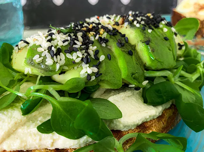 Nahaufnahme von Avocadoscheiben mit Sesam auf Hummus und Röstbrot mit Feldsalat