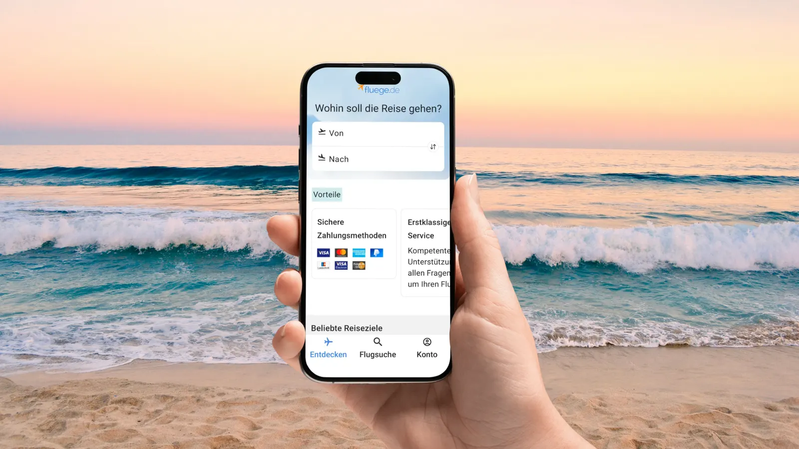 Hand hält ein Smartphone mit der Flugsuche von fluege.de vor einem Strand bei Sonnenuntergang