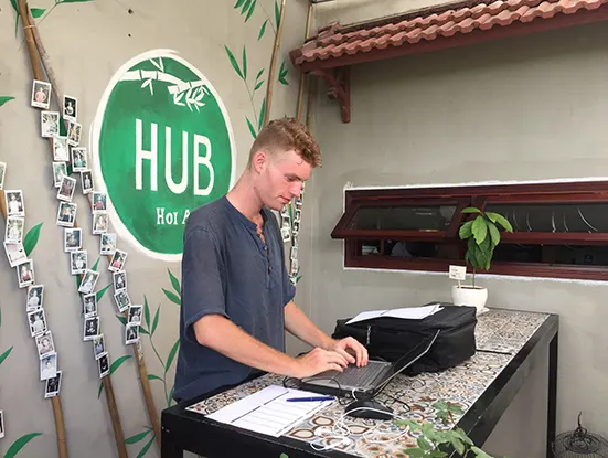 Mann arbeitet im Stehen am Laptop vor einer Wandmalerei mit Hub-Hoi-An-Logo