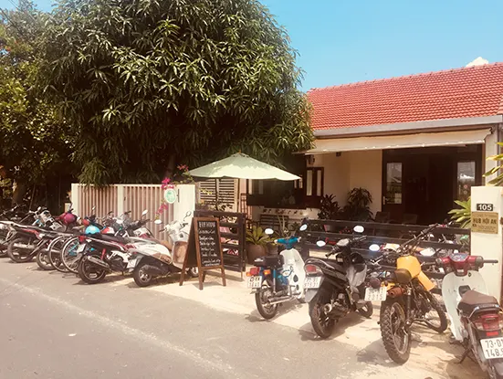 Straßenansicht des Coworking-Hauses mit rotem Ziegeldach, Sonnenschirm und vielen geparkten Motorrollern