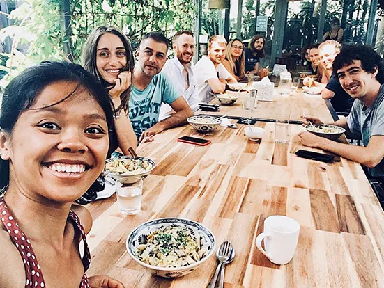 Gruppen-Selfie beim gemeinsamen Mittagessen an einem langen Holztisch mit Nudelschalen