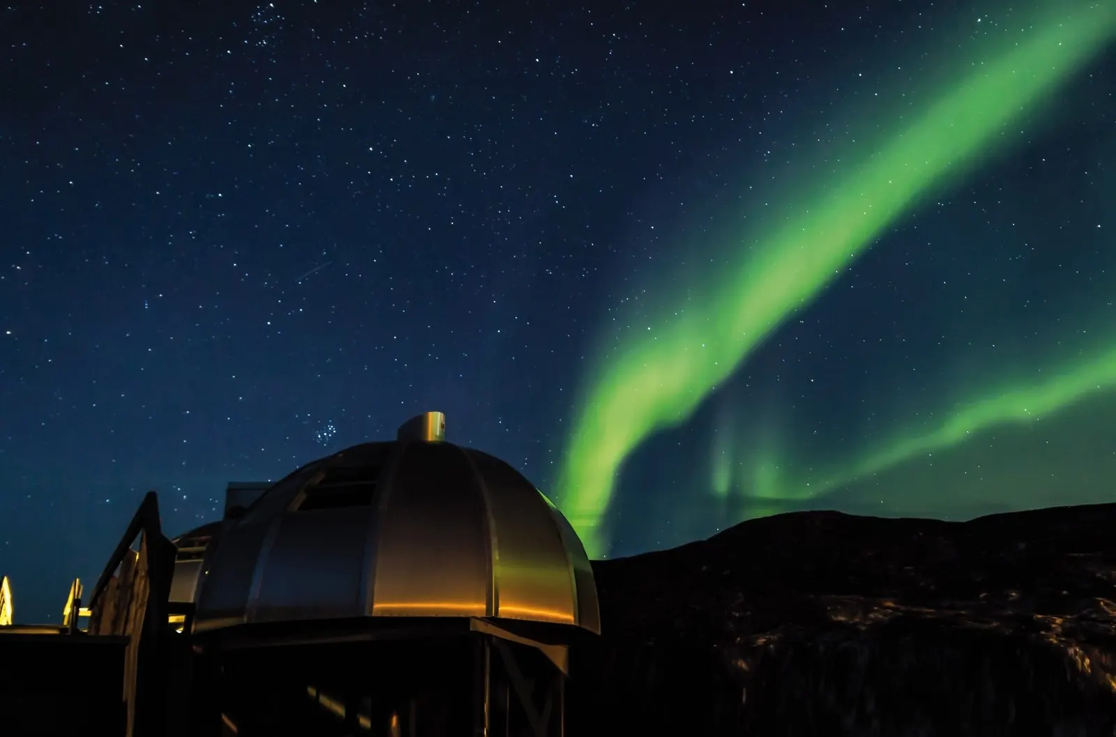 Grüne Nordlichtbänder über einer beleuchteten Iglu-Kuppel im Sternenhimmel