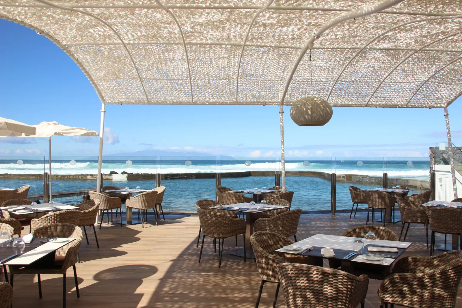 Restaurantterrasse unter hellem Geflechtdach mit Korbstühlen direkt an der Meeresbrandung