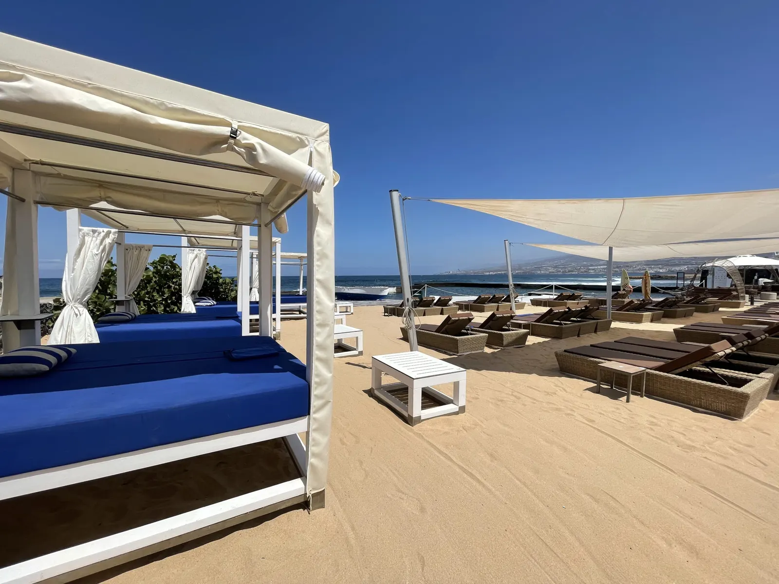 Beachclub mit blau bezogenen Himmelbetten und Liegereihen auf hellem Sand am Meer