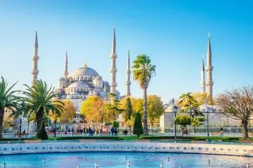 Blaue Moschee mit Kuppeln und sechs Minaretten hinter Palmen und Springbrunnen