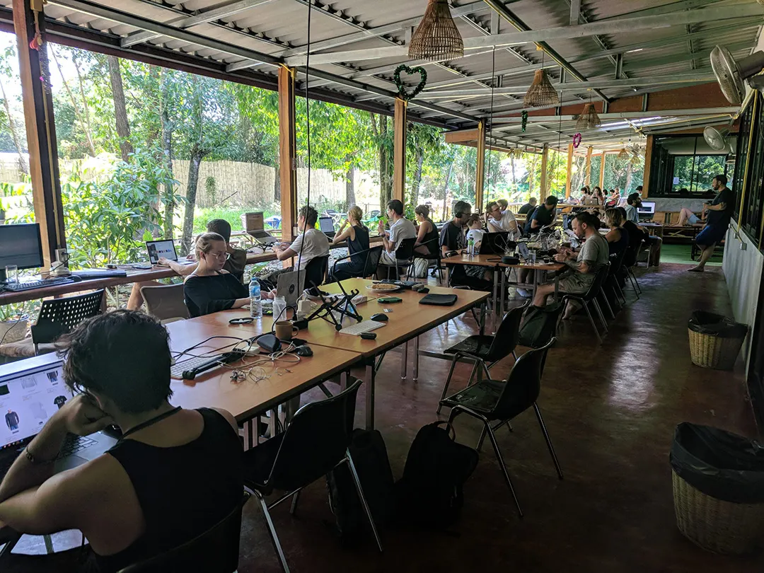 Voll belegte Tischreihen mit Laptops in einem offenen Coworking-Space am Garten