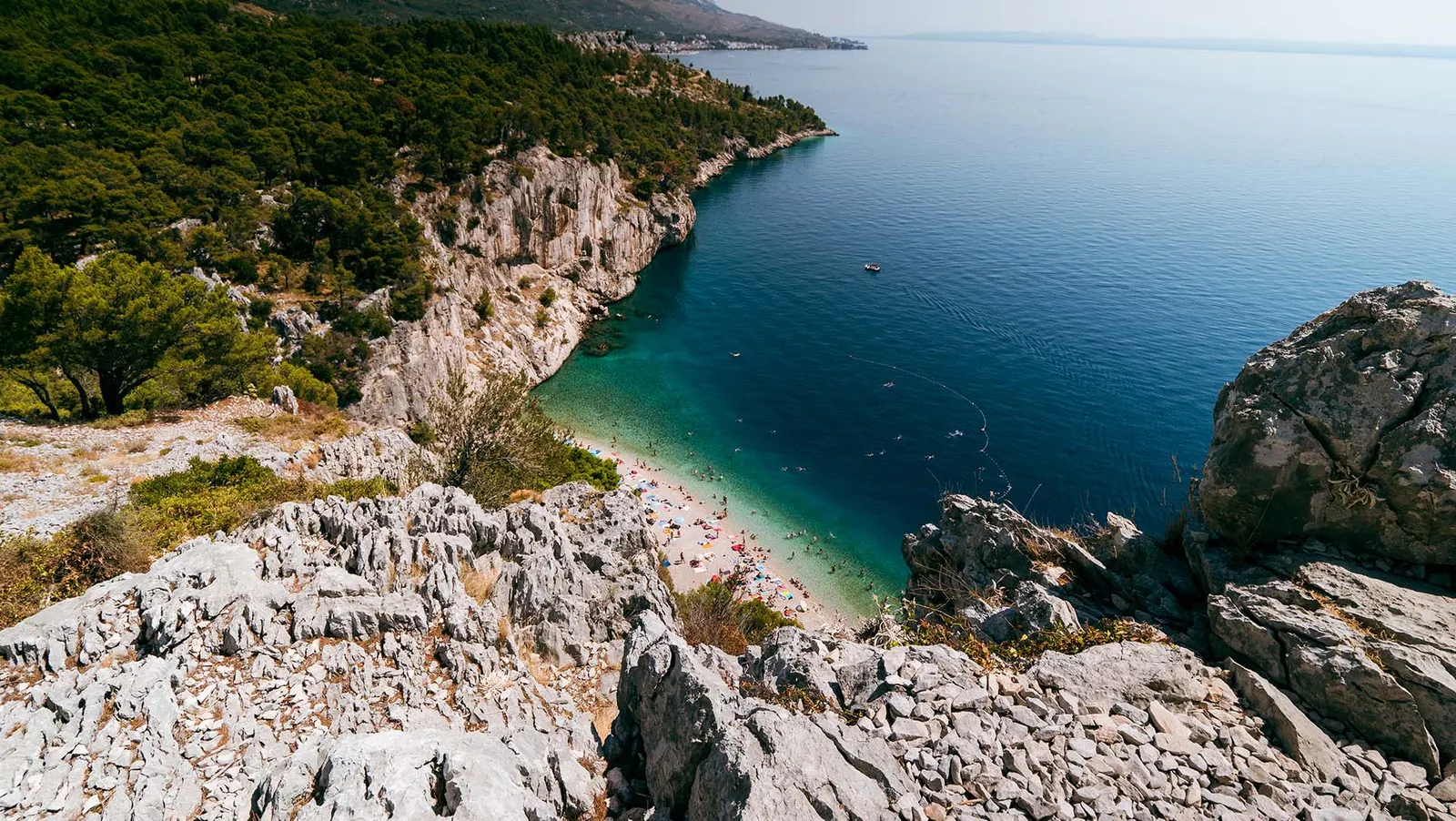 Blick von Felsen auf eine Bucht mit Kiesstrand, Pinien und tiefblauem Meer