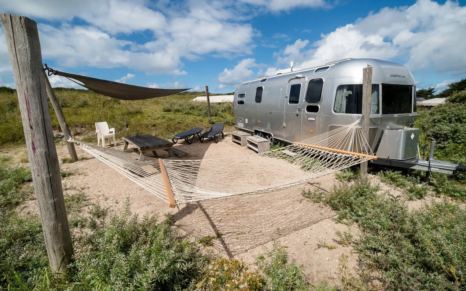 Airstream-Wohnwagen auf einem Sandplatz mit Hängematte, Sonnensegel und Liegestühlen