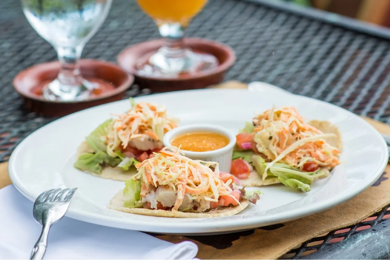 Drei Tortillas mit Krautsalat und Dip auf weißem Teller, daneben Bier und Wasserglas
